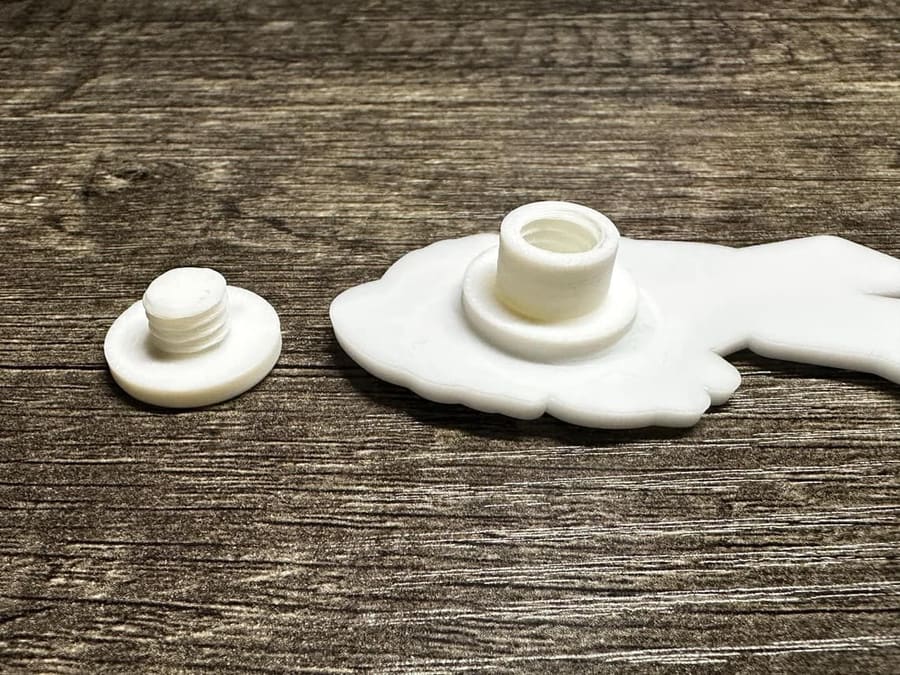 Close-up of a white screw-on charm backer and its threaded post on a wood surface