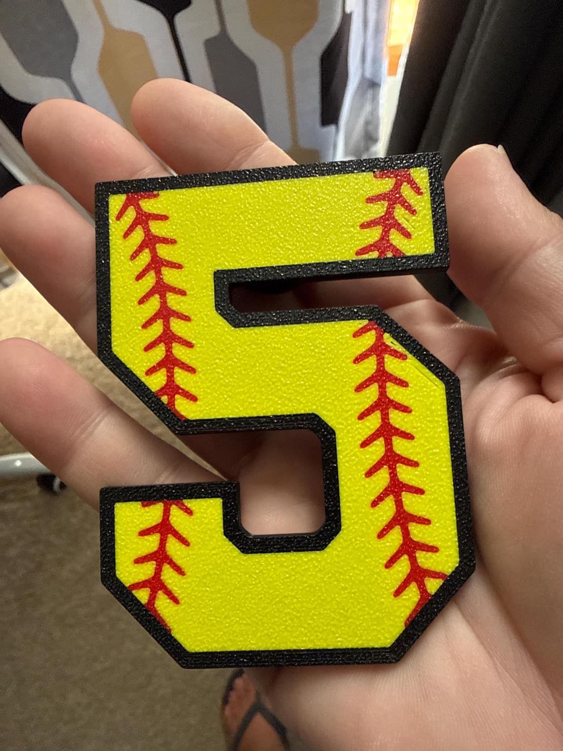 Yellow softball number 5 charm with red stitching held in an open hand