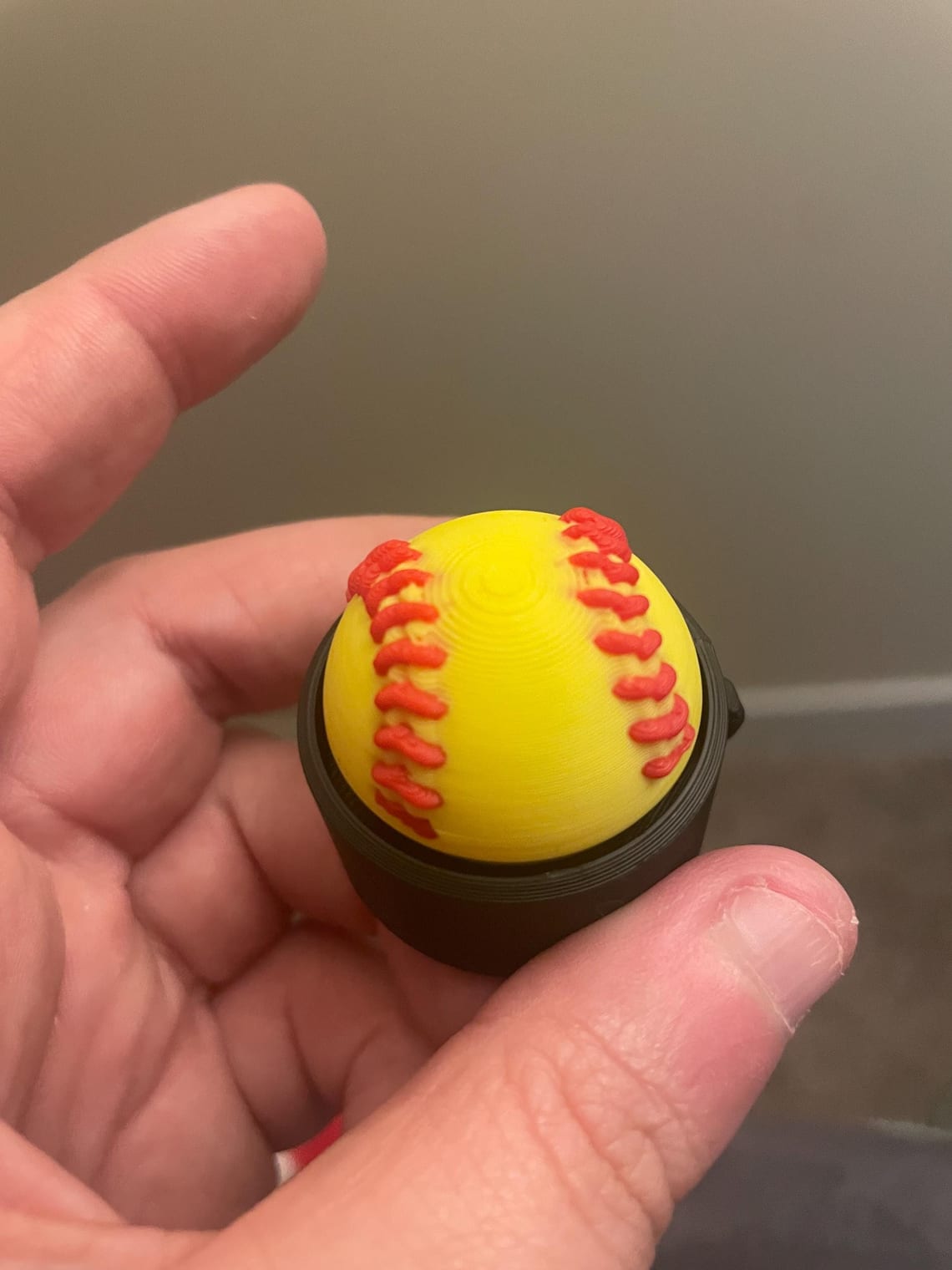 Yellow softball clicker fidget with red stitching held between two fingers