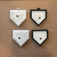 Four 3D printed home plate fidget toys in white and black, each with nested moving layers, on a cardboard surface