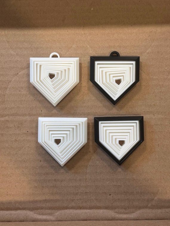 Four 3D printed home plate fidget toys in white and black, each with nested moving layers, on a cardboard surface