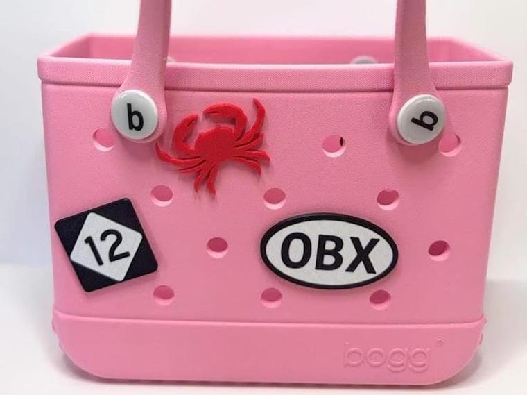 Pink Bogg Bag with a black and white OBX oval charm, red crab charm, and number 12 charm attached