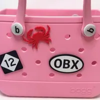 Pink Bogg Bag with a black and white OBX oval charm, red crab charm, and number 12 charm attached